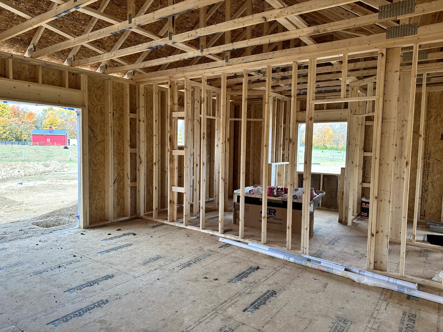 Exposed wood framing and beams inside a partially constructed room with unfinished floor and visible insulation.