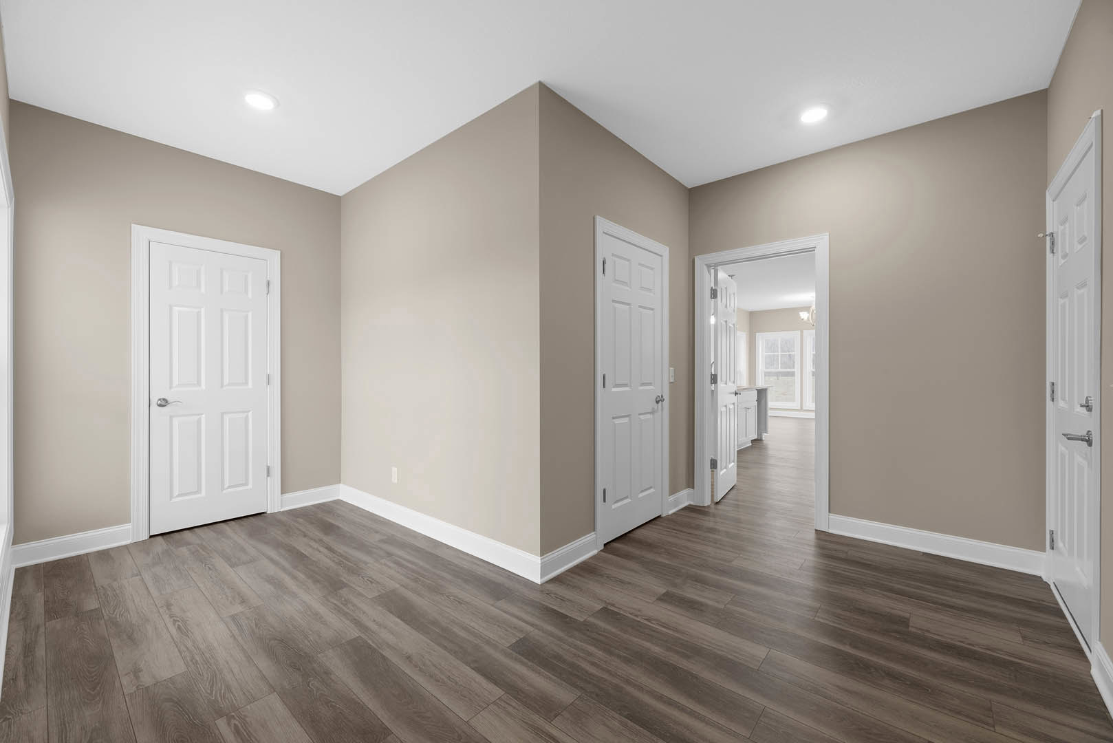 Hallway with white paneled doors featuring silver handles, light wood flooring, and white baseboard trim