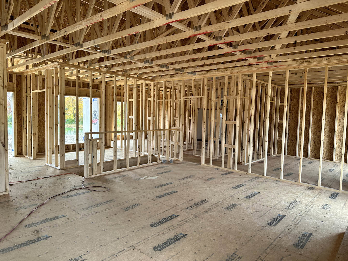 Exposed wooden beams and framing inside a house under construction, unfinished floor and ceiling visible