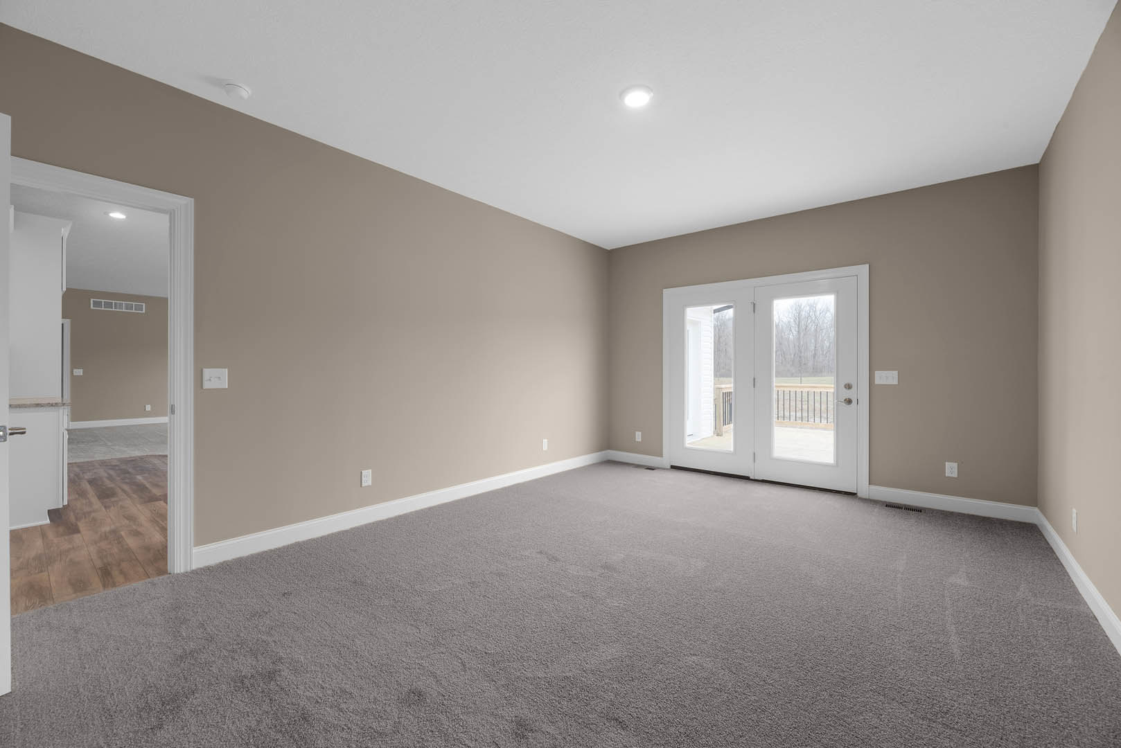 White double doors with glass panes open into a carpeted room, featuring white walls, ceiling light fixture, and decorative molding.
