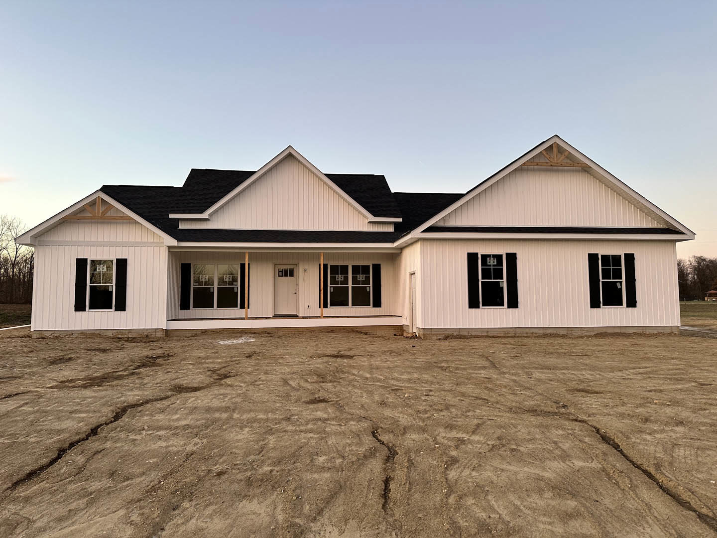 Modern house with black roof, white siding, glass-paned windows, and white door, surrounded by dirt yard with visible ground crack