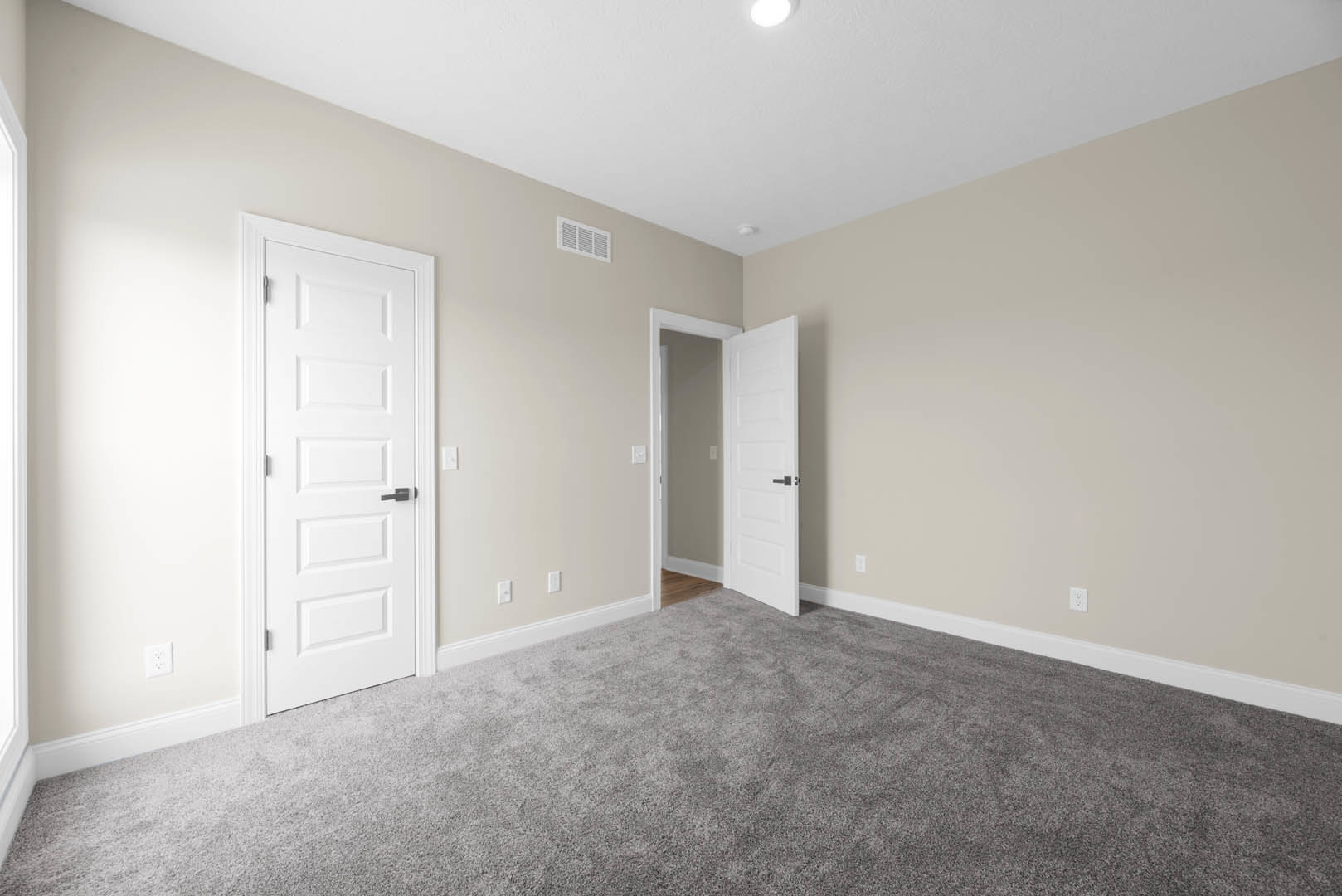 Grey carpeted floor in a room with white paneled doors featuring black and silver handles, white walls, and a visible light switch