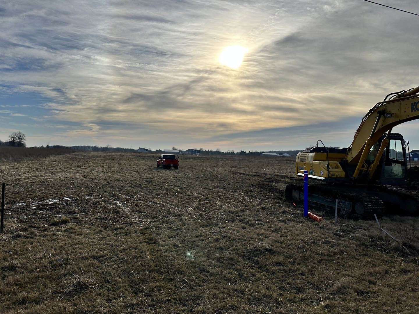 Yellow bulldozer and red tractor parked on grassy field under partly cloudy sky, sunlight streaming through clouds