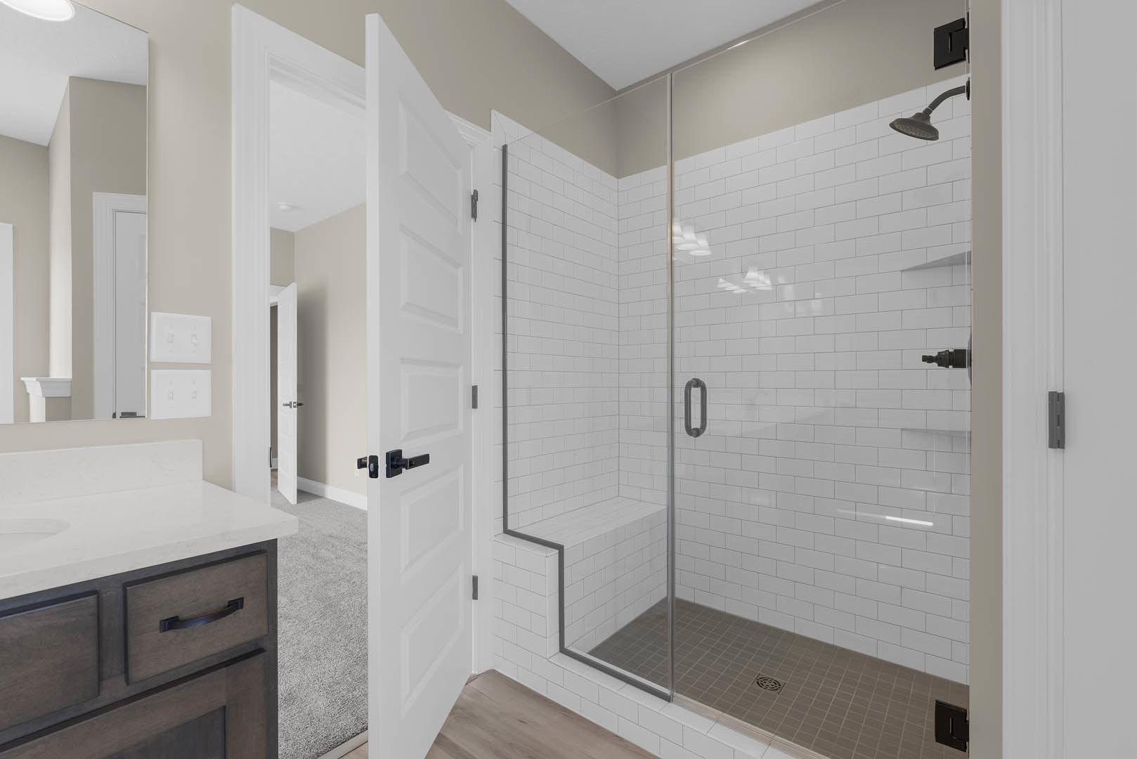 Modern bathroom featuring a glass shower enclosure, tiled shower floor with central drain, light wood cabinetry with sleek drawer fronts, and matte black rectangular hardware.