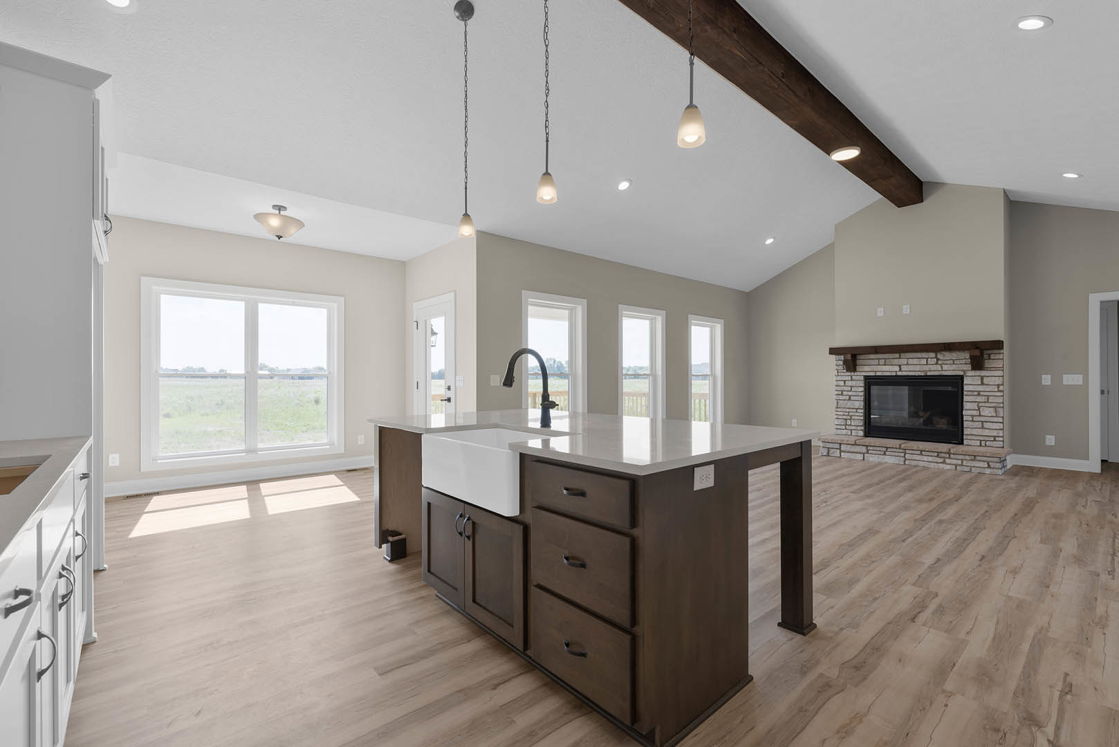 Kitchen with a central island featuring drawers and a sink, curved neck faucet, pendant lights overhead, black and glass fireplace, cabinetry, laminate flooring, and a window