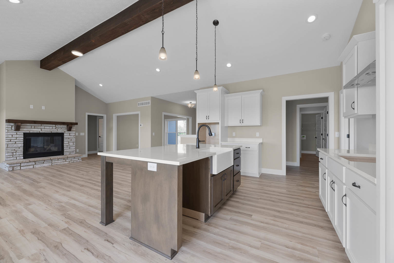 Open-concept kitchen and dining area featuring a large white island with black pendant lights, white cabinetry with silver handles, brick accent wall with window, glass-front