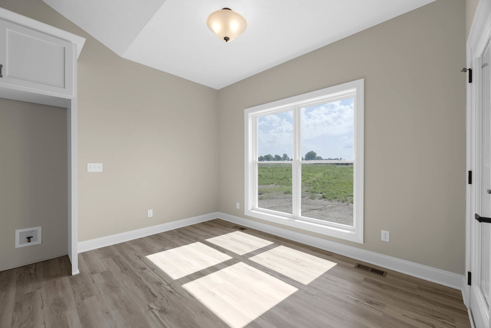 Sunlit room featuring wide wood plank flooring, large window overlooking grassy field, white walls with crown molding, modern ceiling light with white shade, and white door with