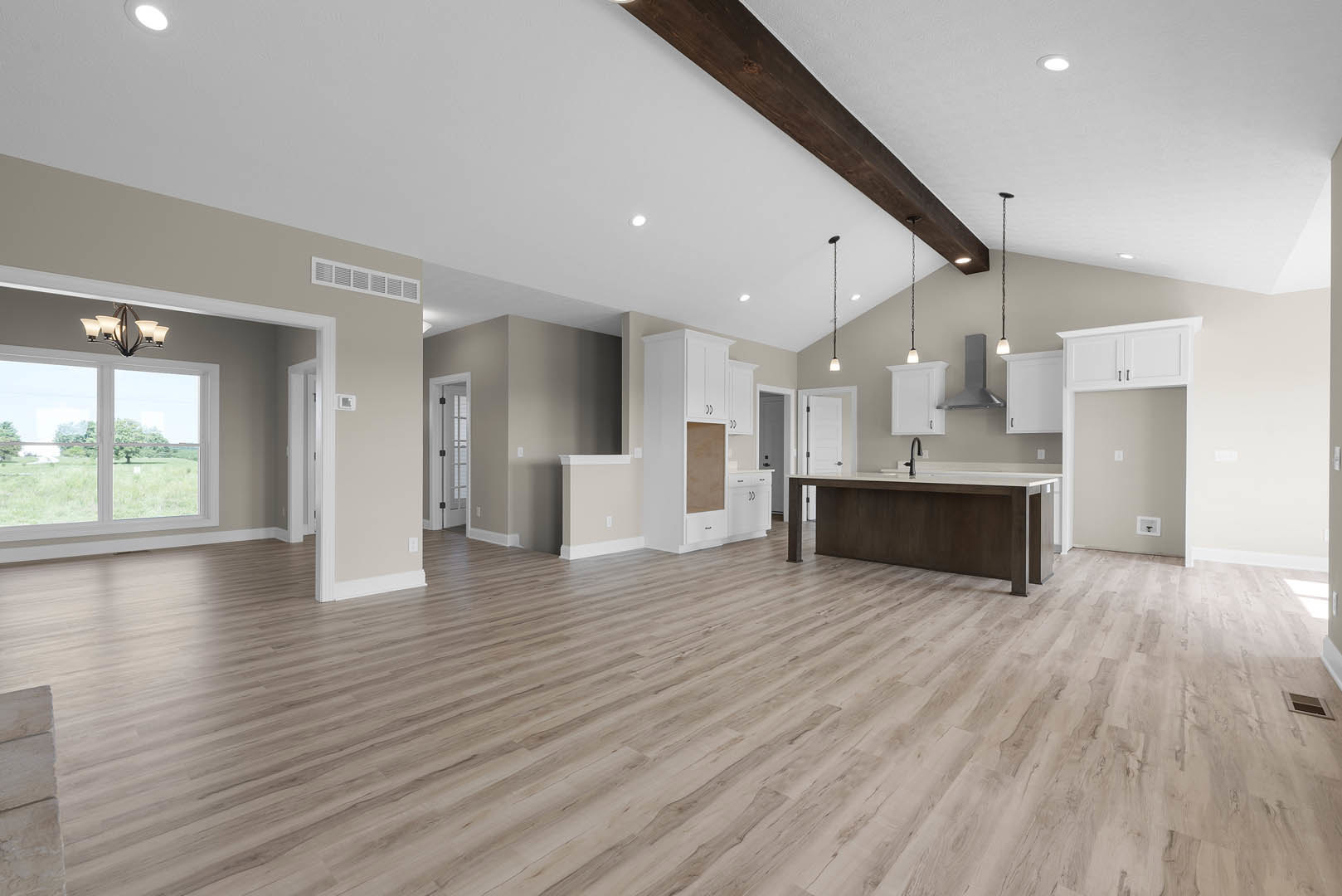 Spacious open kitchen and dining area with hardwood floors, white walls, black pendant lamp above a wide counter, large window overlooking a grassy field, close-up of modern light