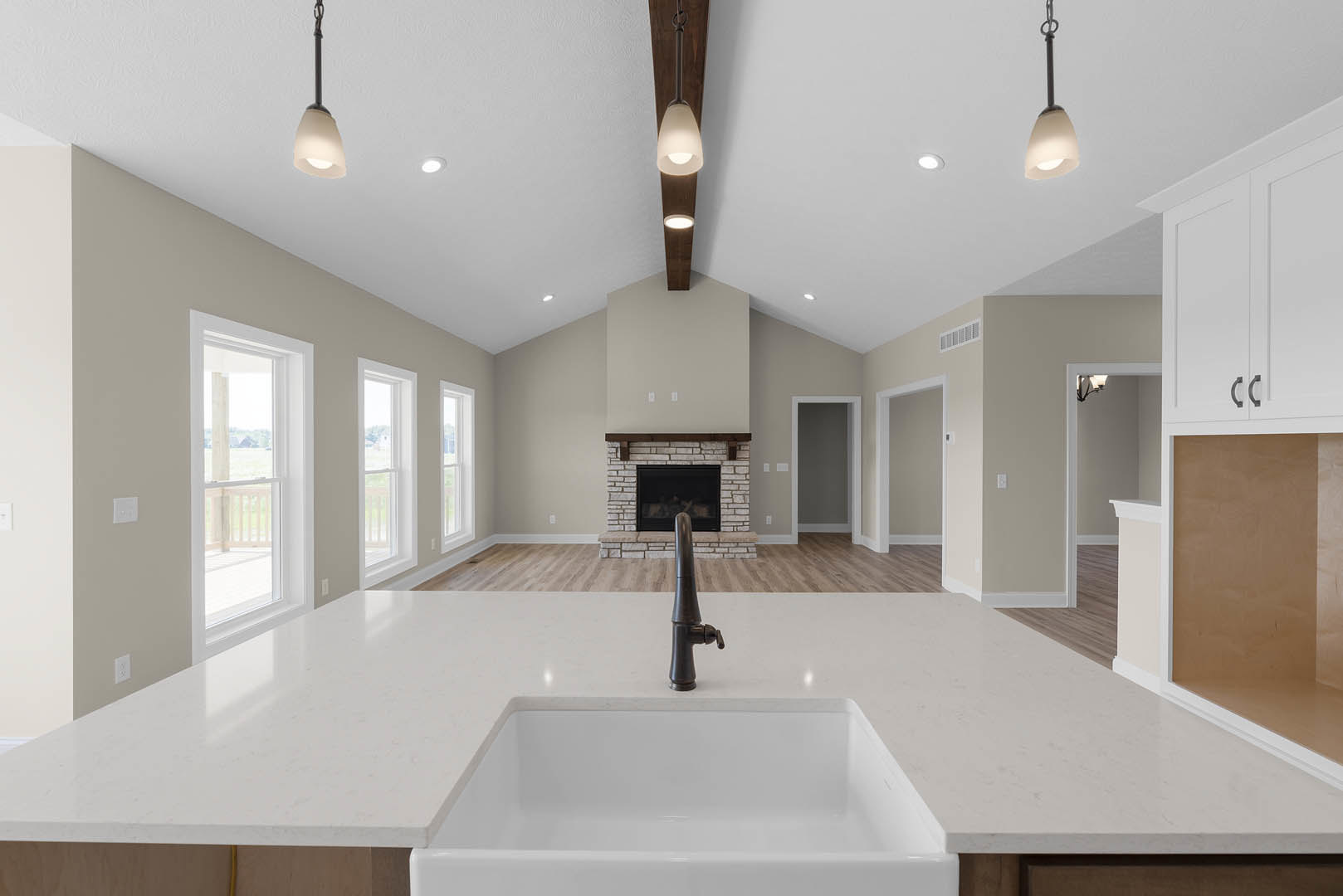 Open kitchen with white cabinetry, stone countertop, stainless steel sink and faucet, built-in fireplace with black metal surround, light wood flooring, and recessed ceiling