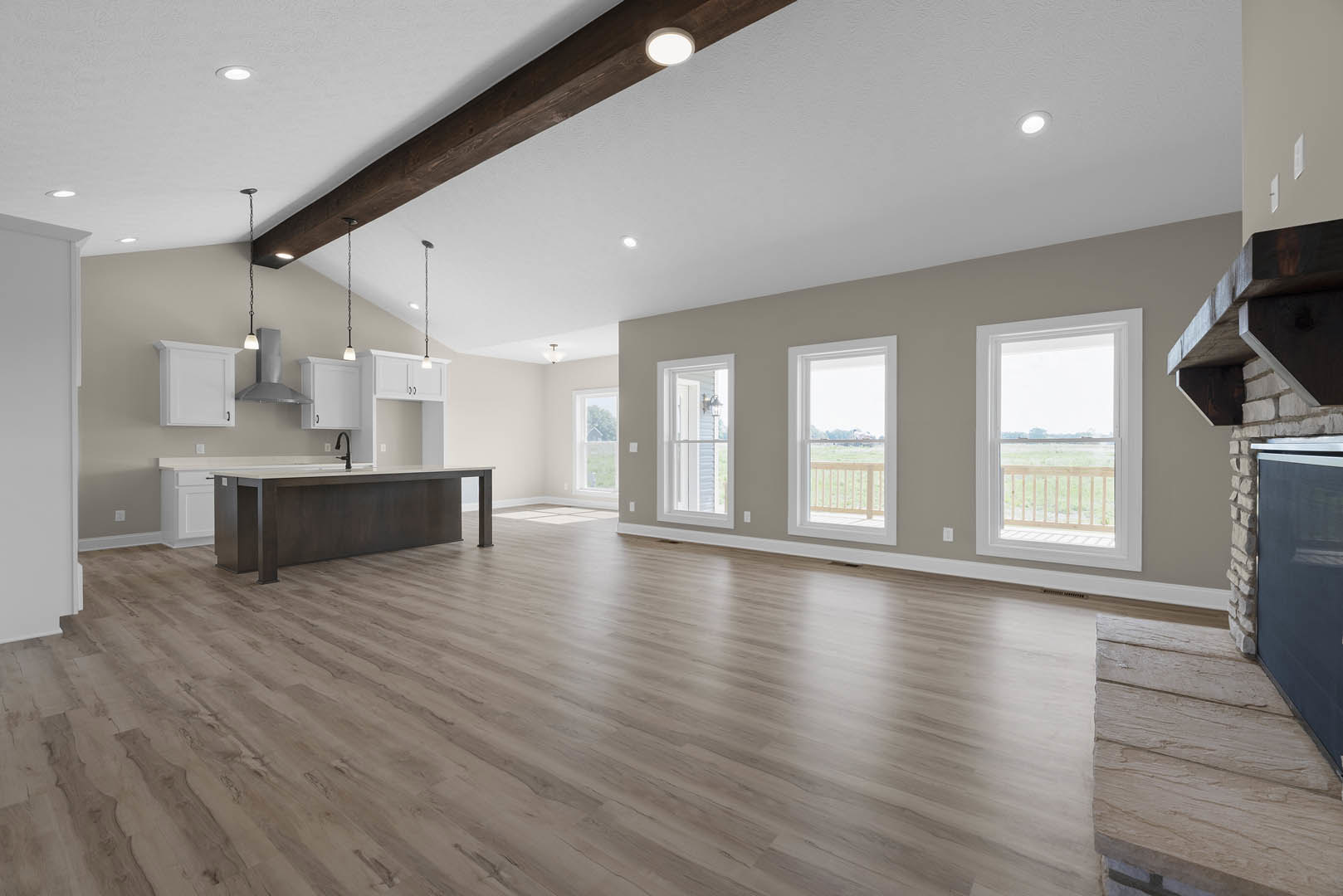Spacious kitchen with wood flooring, central island featuring a sink, white cabinetry, recessed ceiling lights, large windows overlooking a grassy field, and a lamp placed on the