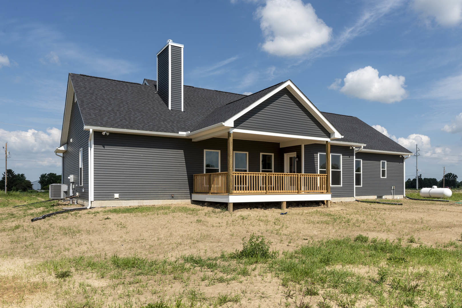 Two-story house with covered porch, wooden railing, white-framed windows, and grassy lawn under partly cloudy sky