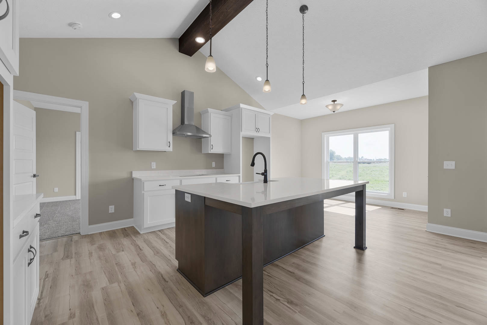 Spacious kitchen featuring a large central island with white cabinetry and black hardware, black faucet, light countertops, wood flooring, and a window providing natural light.
