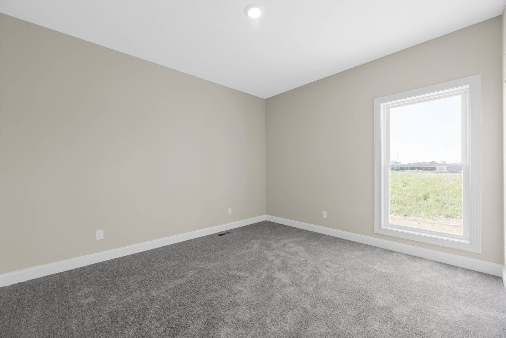 White ceiling with recessed light, grey carpeted floor, large window overlooking green grass, neutral walls, simple molding.