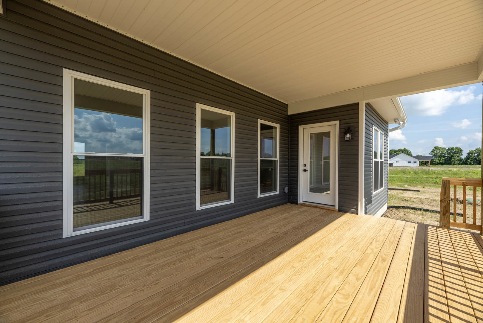 Two-story home with white-framed windows, wooden deck, covered porch, and landscaped yard with trees