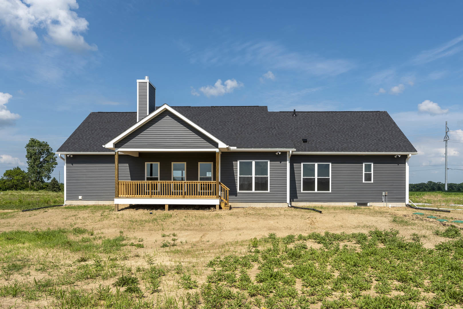 White siding house with covered porch, wooden railing, large windows, and manicured green lawn under partly cloudy sky