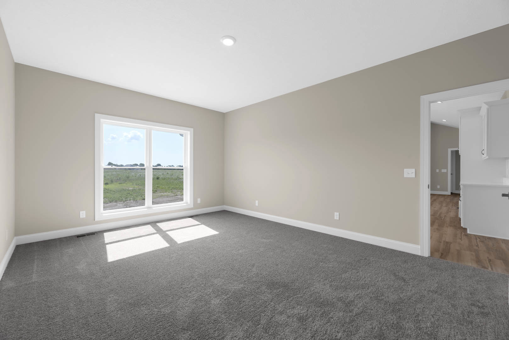 Bedroom with grey carpet, white walls, large window overlooking grassy field, recessed ceiling light, white baseboards, and hardwood floor near built-in white cabinets