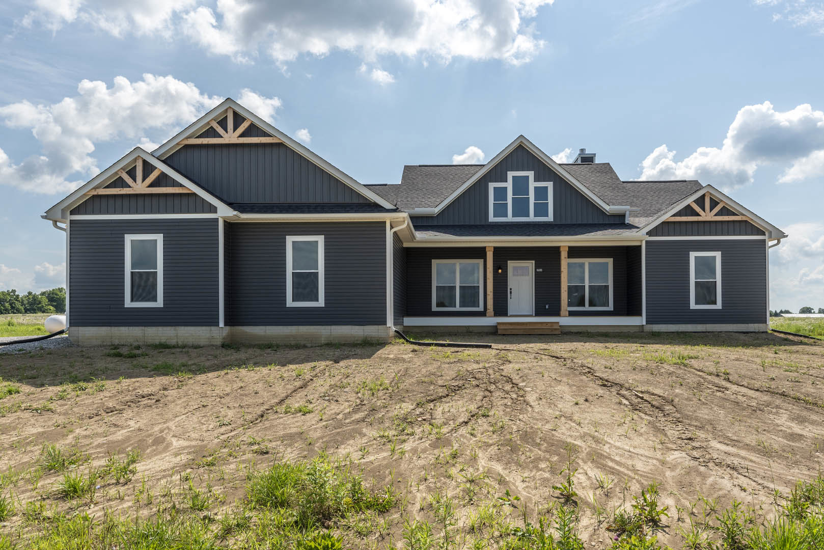 Two-story house with white door and black handle, white-framed windows, surrounded by a dirt field and hose under cloudy sky