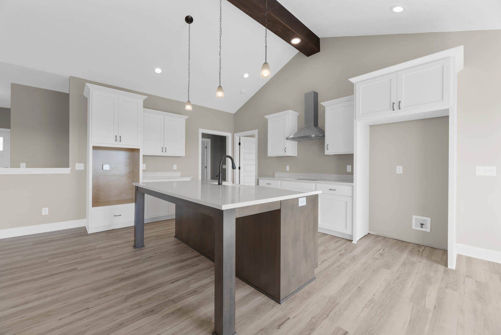 Spacious kitchen featuring a large white and brown island with quartz countertop, stainless steel faucet, white cabinetry, light wood flooring, and recessed lighting on white
