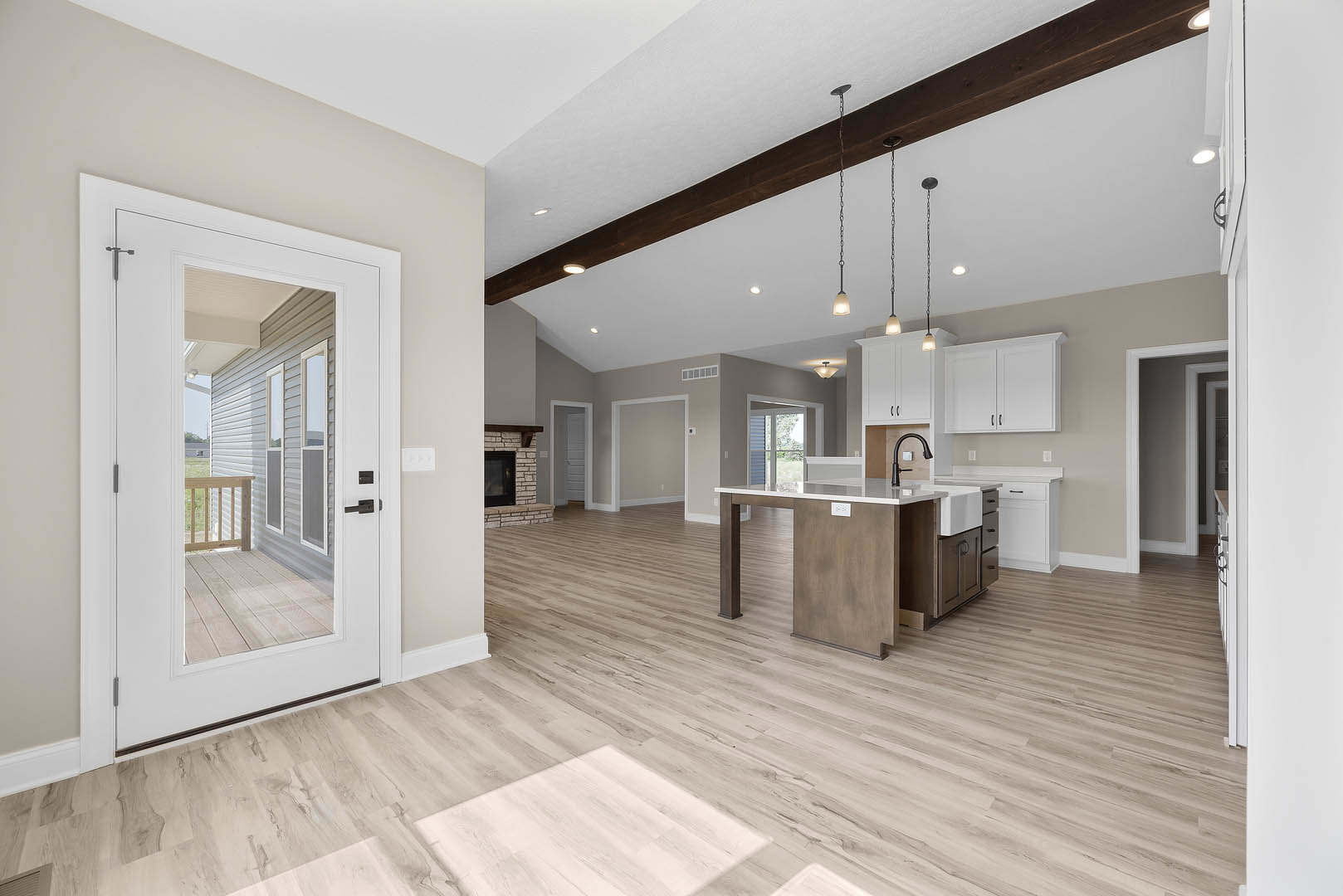 Open-concept kitchen and living room featuring hardwood floors, white cabinets with black handles, black faucet on a kitchen island, dining table, and fireplace; door open to the