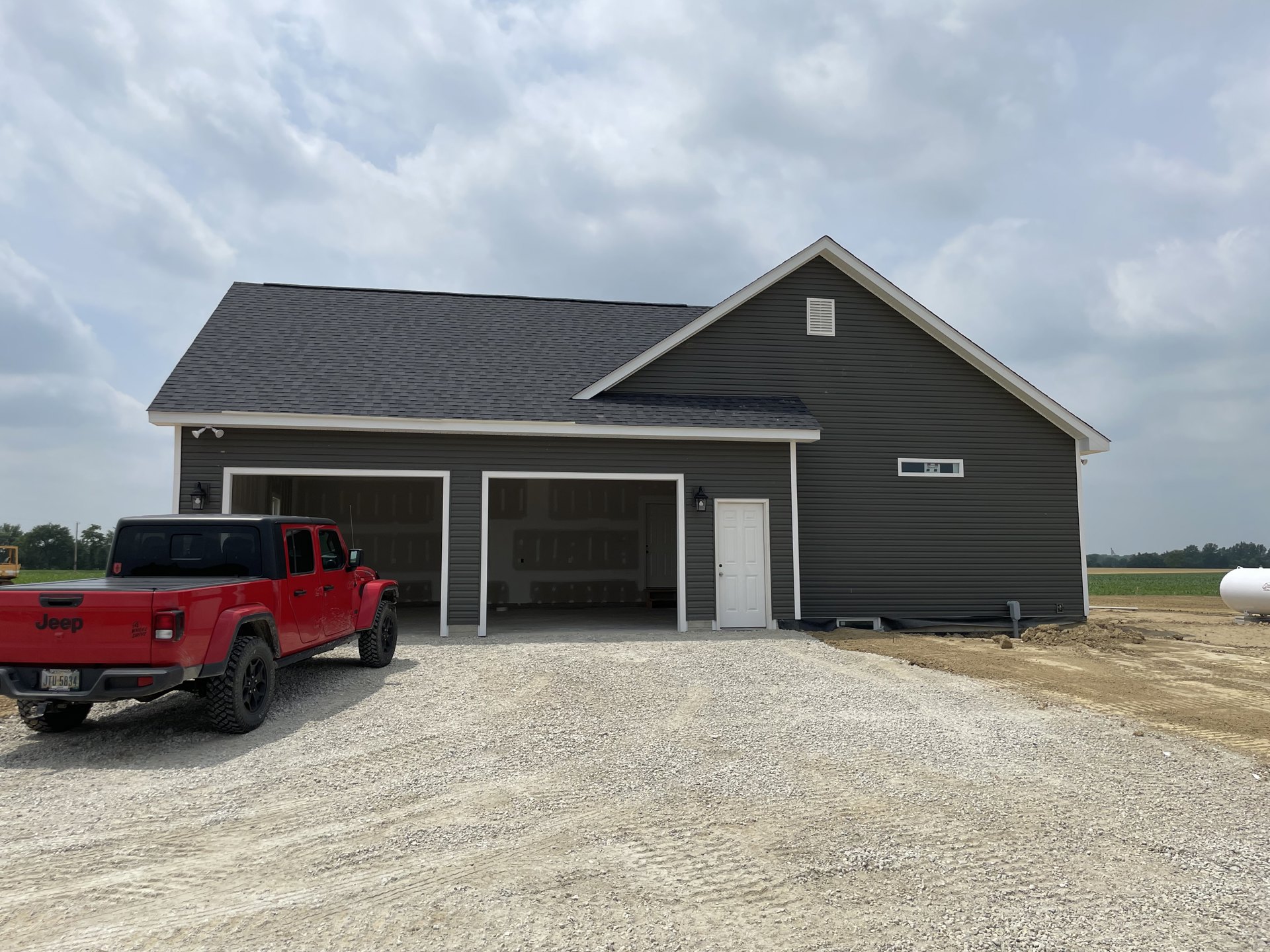 Black siding house with white garage door, gravel driveway, and red pickup truck parked in front