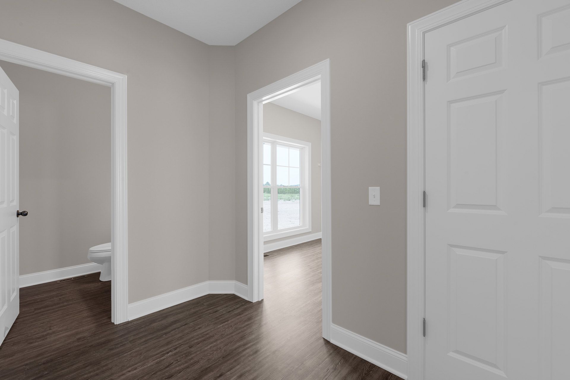 Hallway with white paneled doors, wood laminate flooring, white plaster walls, and a window overlooking a grassy field