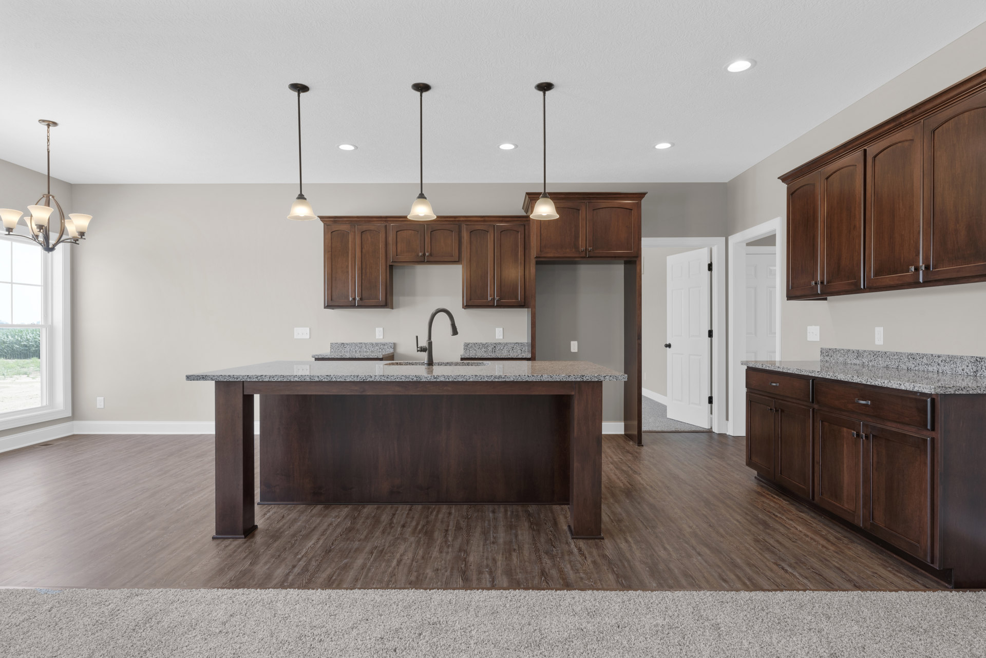 Spacious kitchen featuring a large granite island with built-in sink, white cabinetry, stainless steel appliances, pendant lighting, and hardwood flooring