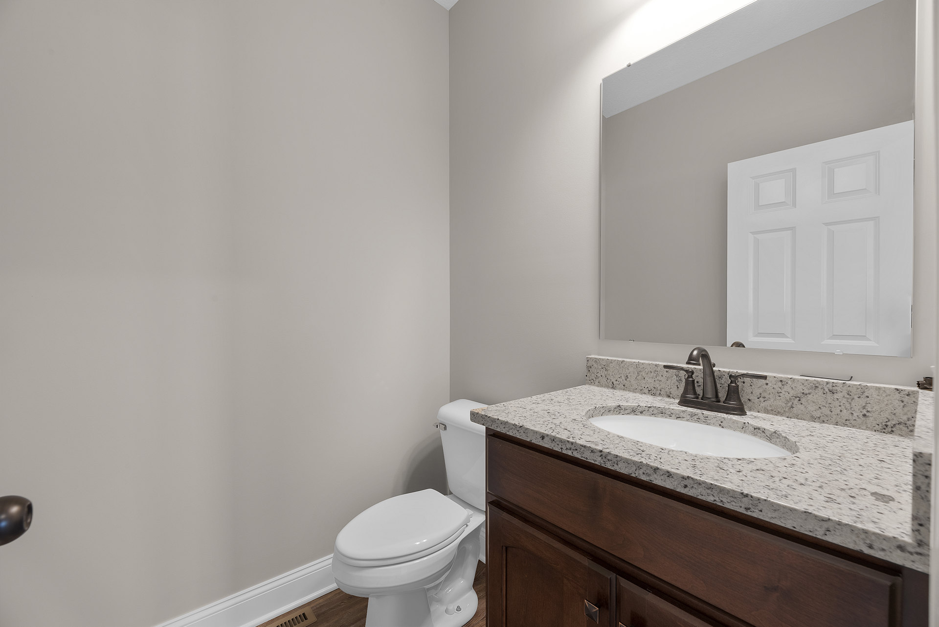 Bathroom with white paneled door, white toilet, wooden vanity with sink and chrome faucet, large mirror above tile backsplash