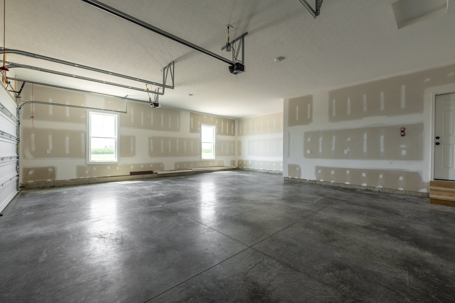 Concrete floor and white painted walls in an empty room with a white-framed window and a ceiling, featuring a close-up of a garage door.