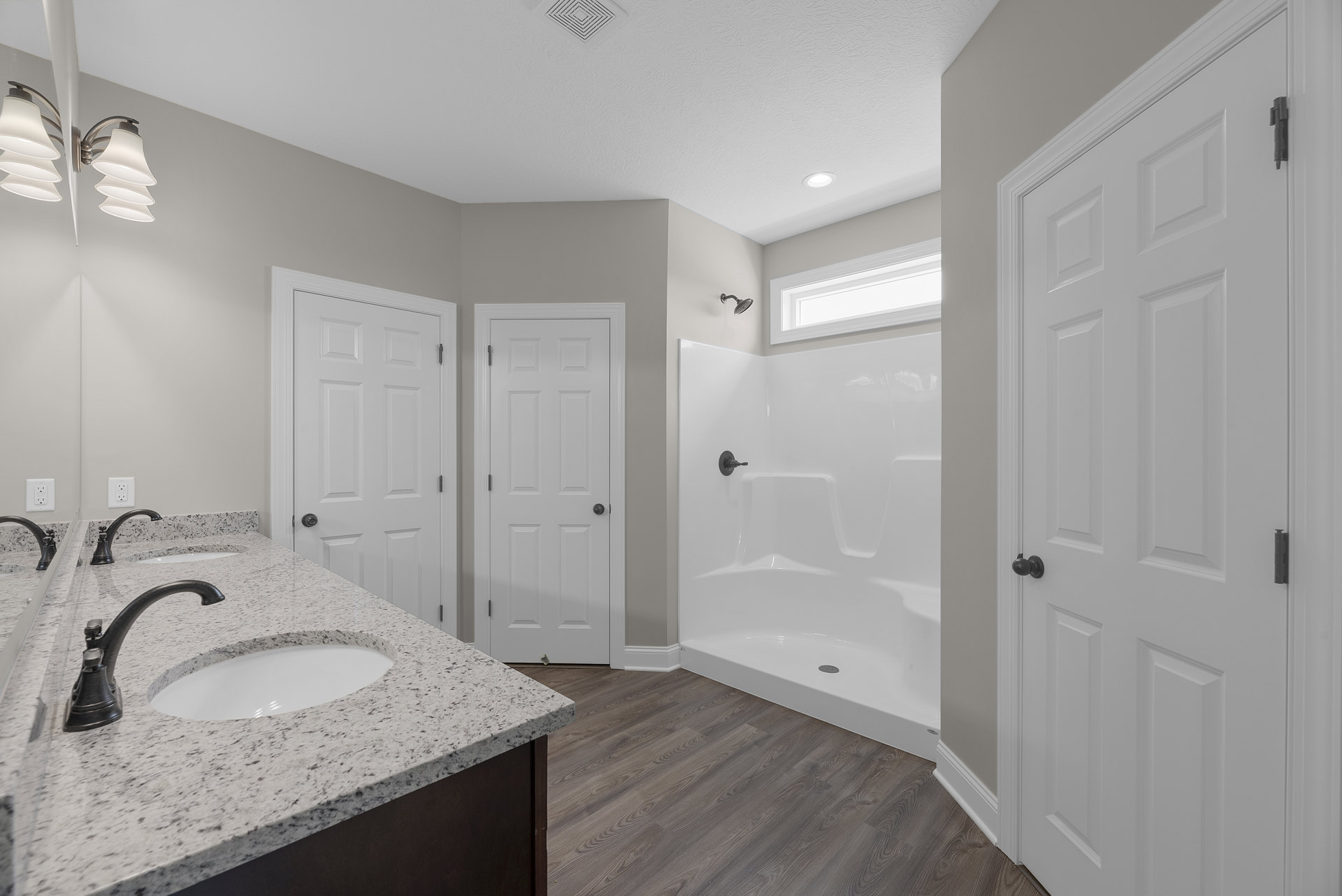 White marble countertop with black faucet and sink, white cabinetry, glass-enclosed shower, white door with black knob, modern multi-bulb light fixture above vanity