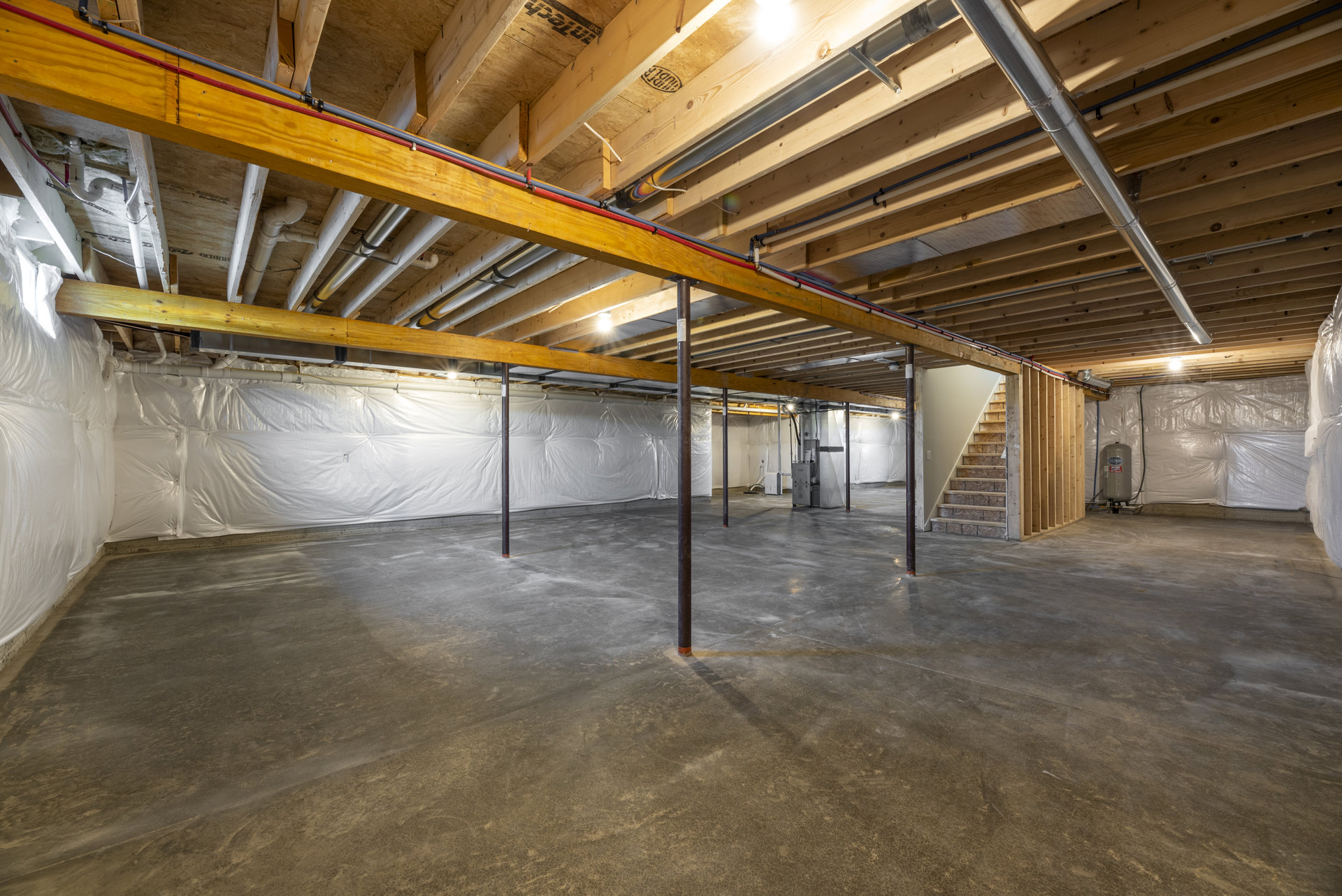 Open-concept room featuring exposed steel beam, concrete floor, modern staircase, and unfinished walls with visible insulation.