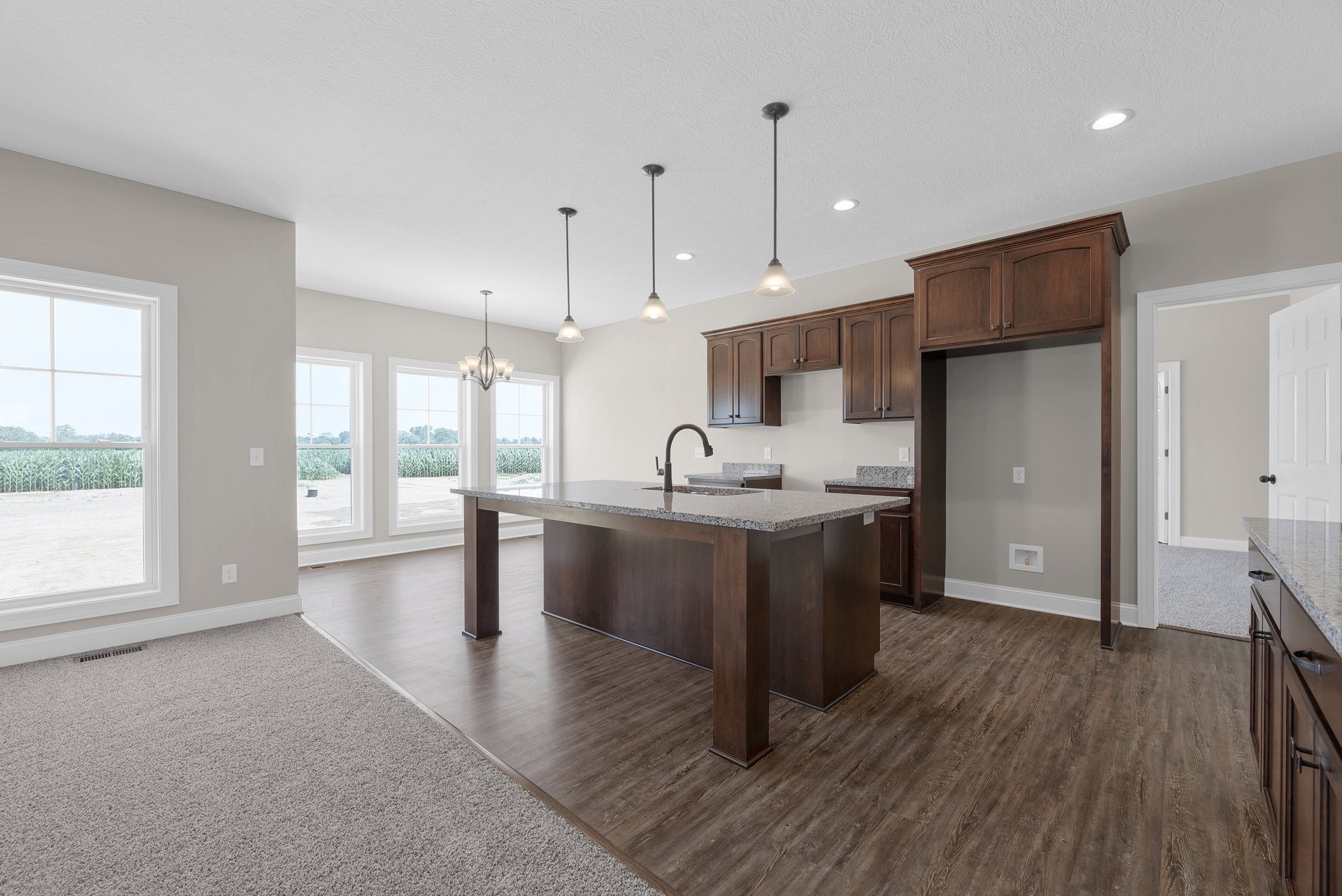 White kitchen with tile backsplash, central island featuring built-in sink and chrome faucet, pendant light fixture overhead, window overlooking corn field, wood cabinetry and