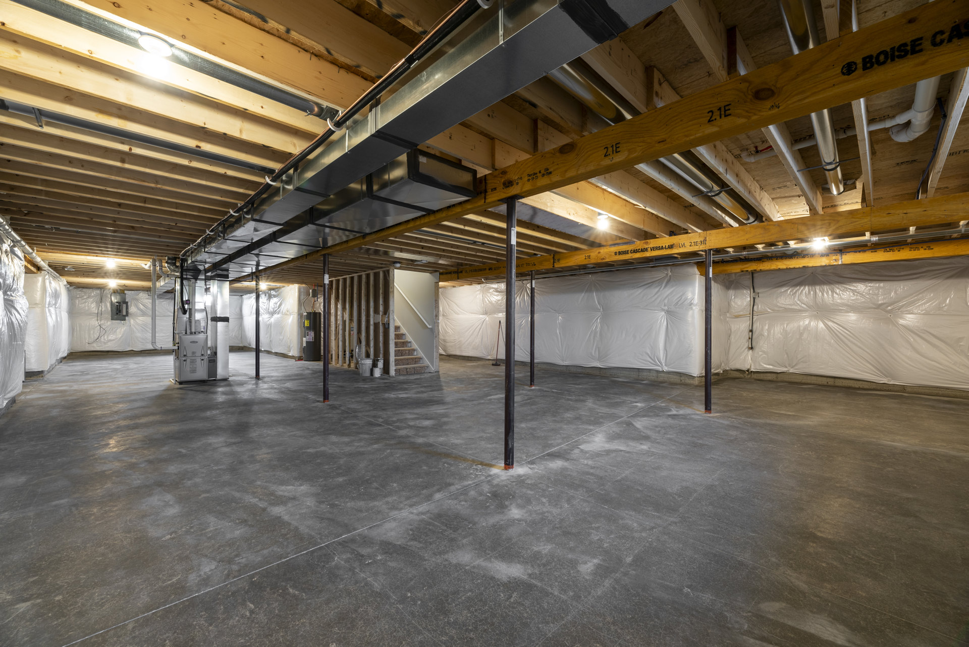 Concrete floor with exposed metal beams overhead, steel support poles, and unfinished wooden framing in an empty basement interior
