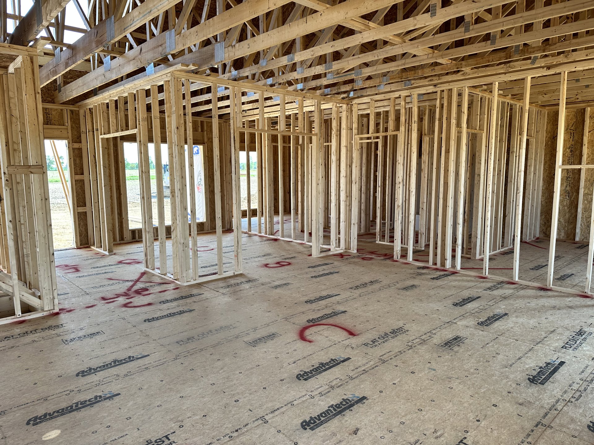 Wooden framing with exposed beams and metal studs inside a house under construction, white floor joists with red paint markings, scattered wooden planks, and a close-up of a red