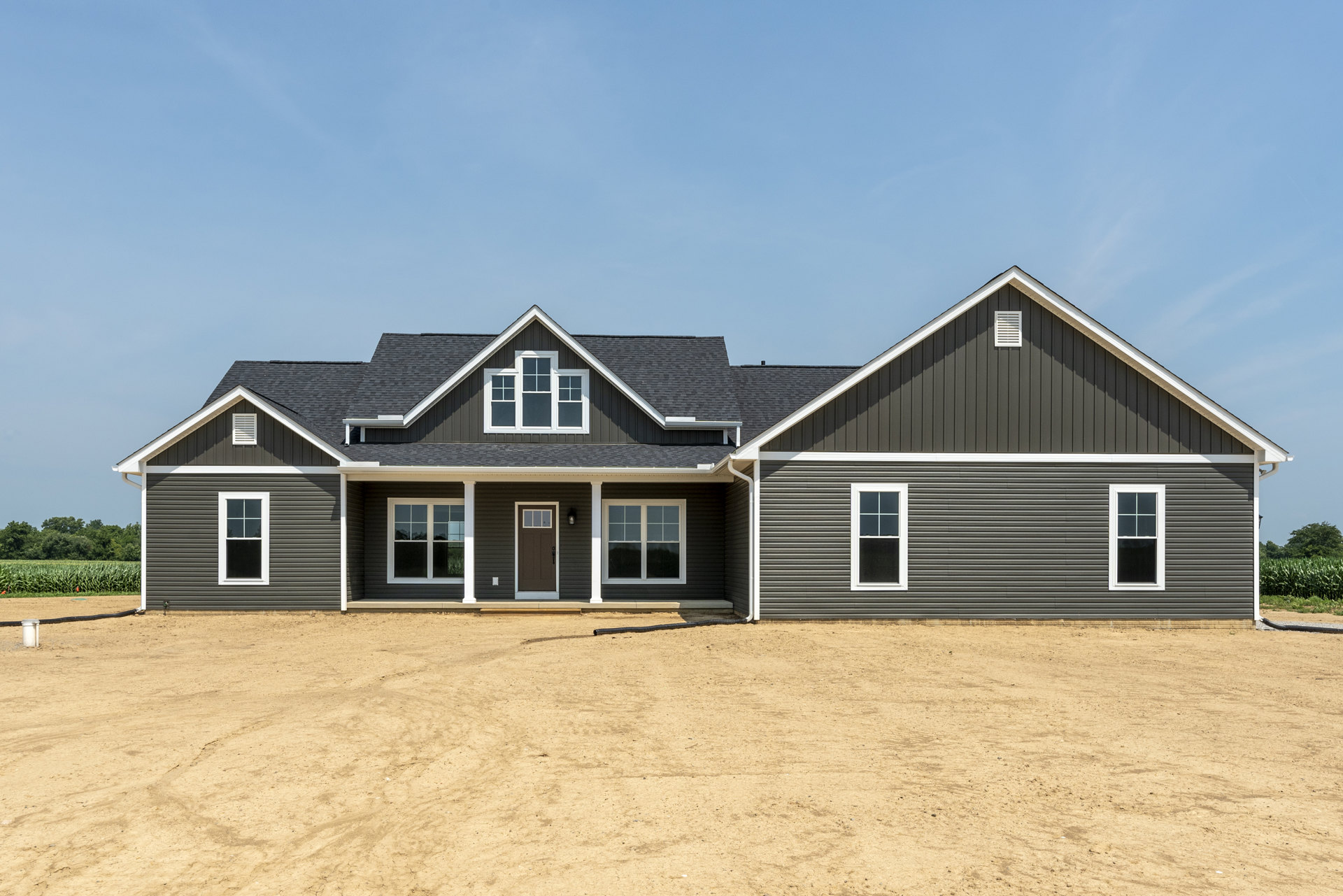 Modern house with light-colored siding, two contrasting framed windows, unfinished dirt yard, and visible black pipe in open garage