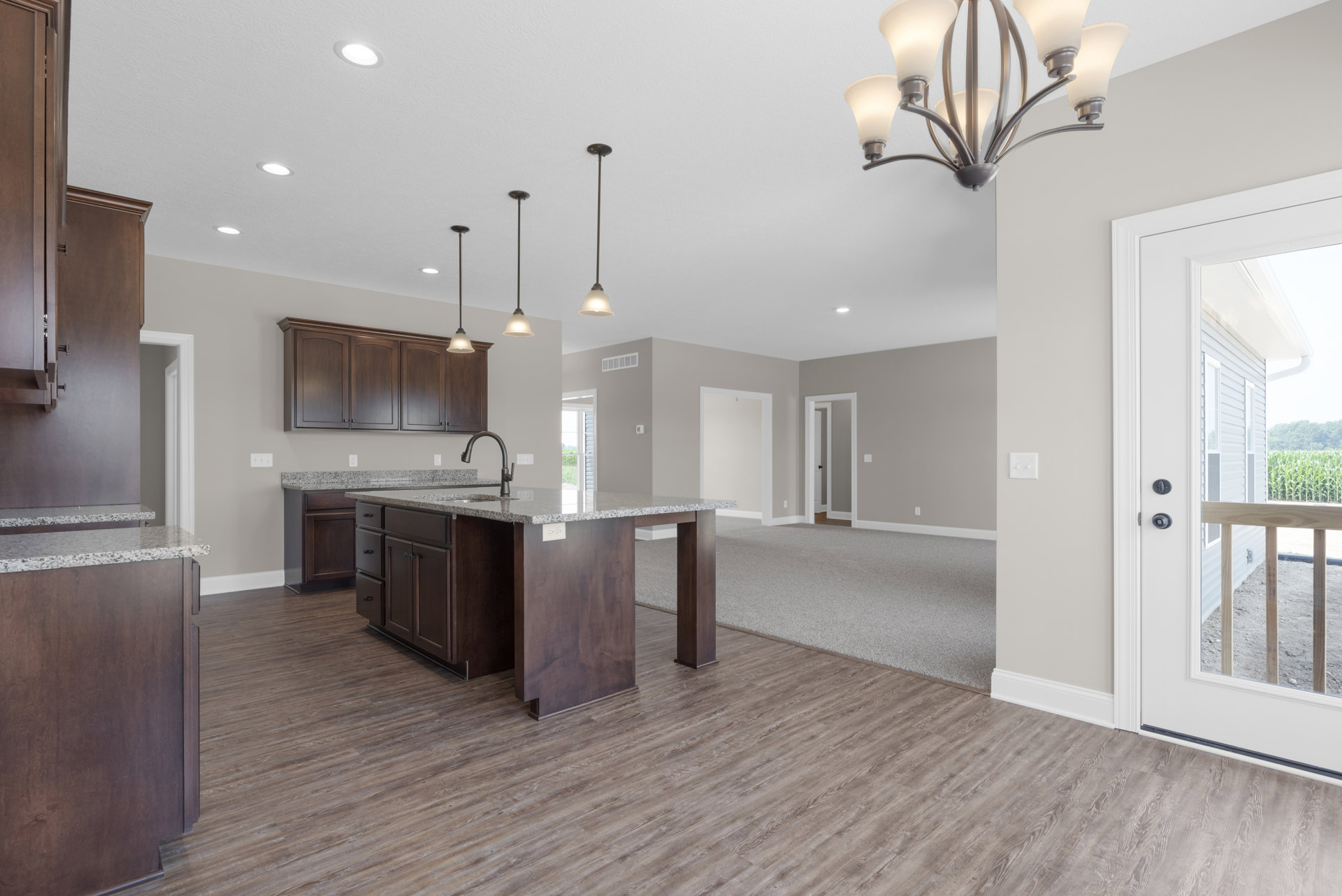 Open-concept kitchen and living room featuring a large chandelier, white cabinetry, wood kitchen island with built-in sink, polished countertops, hardwood flooring, and detailed