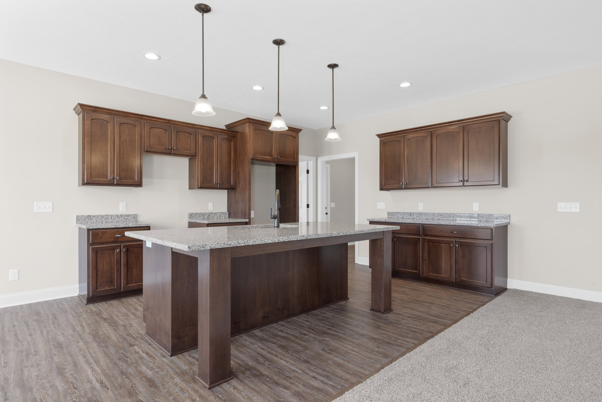 Spacious kitchen featuring a large central island with stone countertop, built-in sink, tile backsplash, wood cabinetry, stainless steel appliances, and pendant lighting.