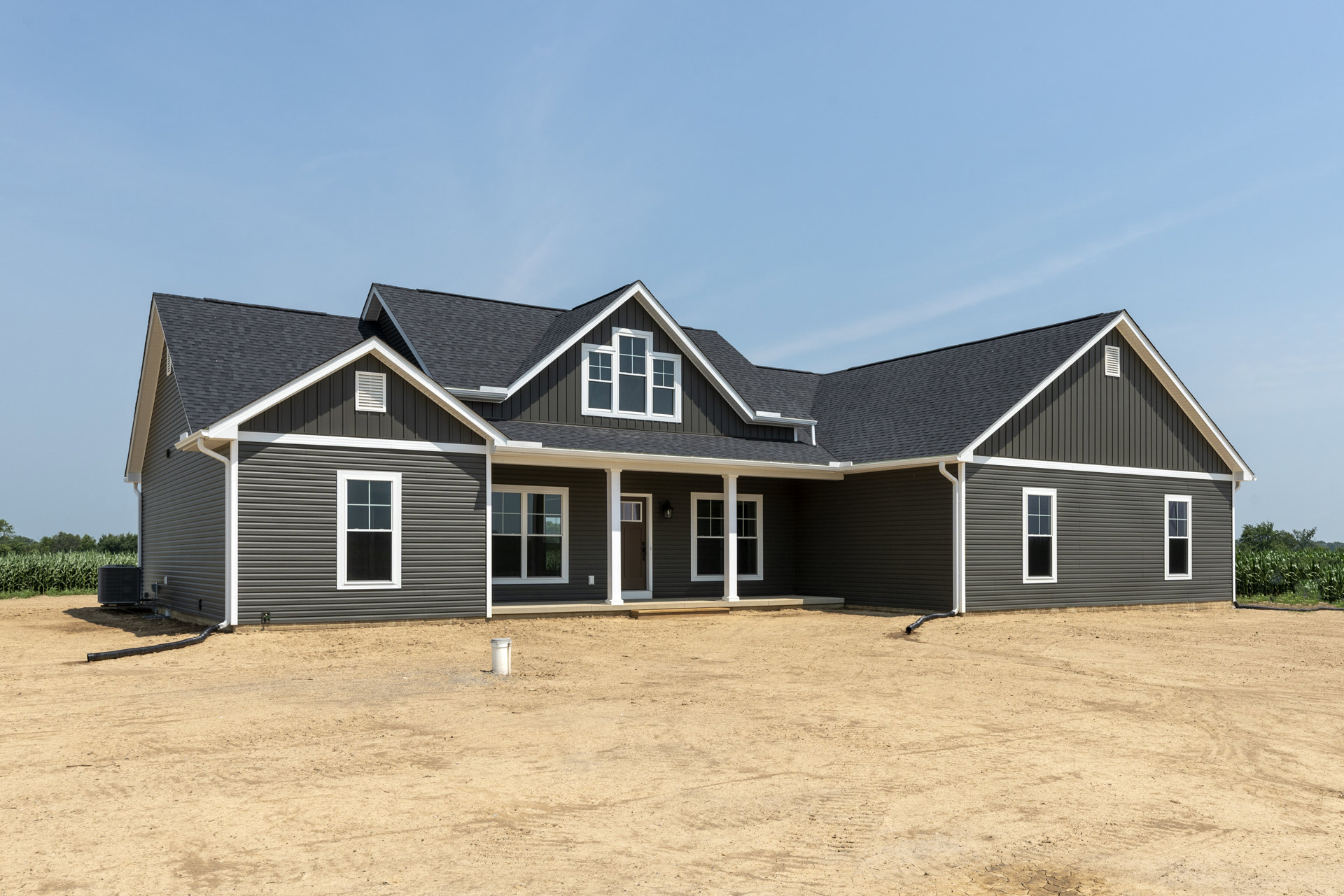 Two-story home with white siding, black-framed windows, covered front porch, white columns, and expansive green lawn under a blue sky