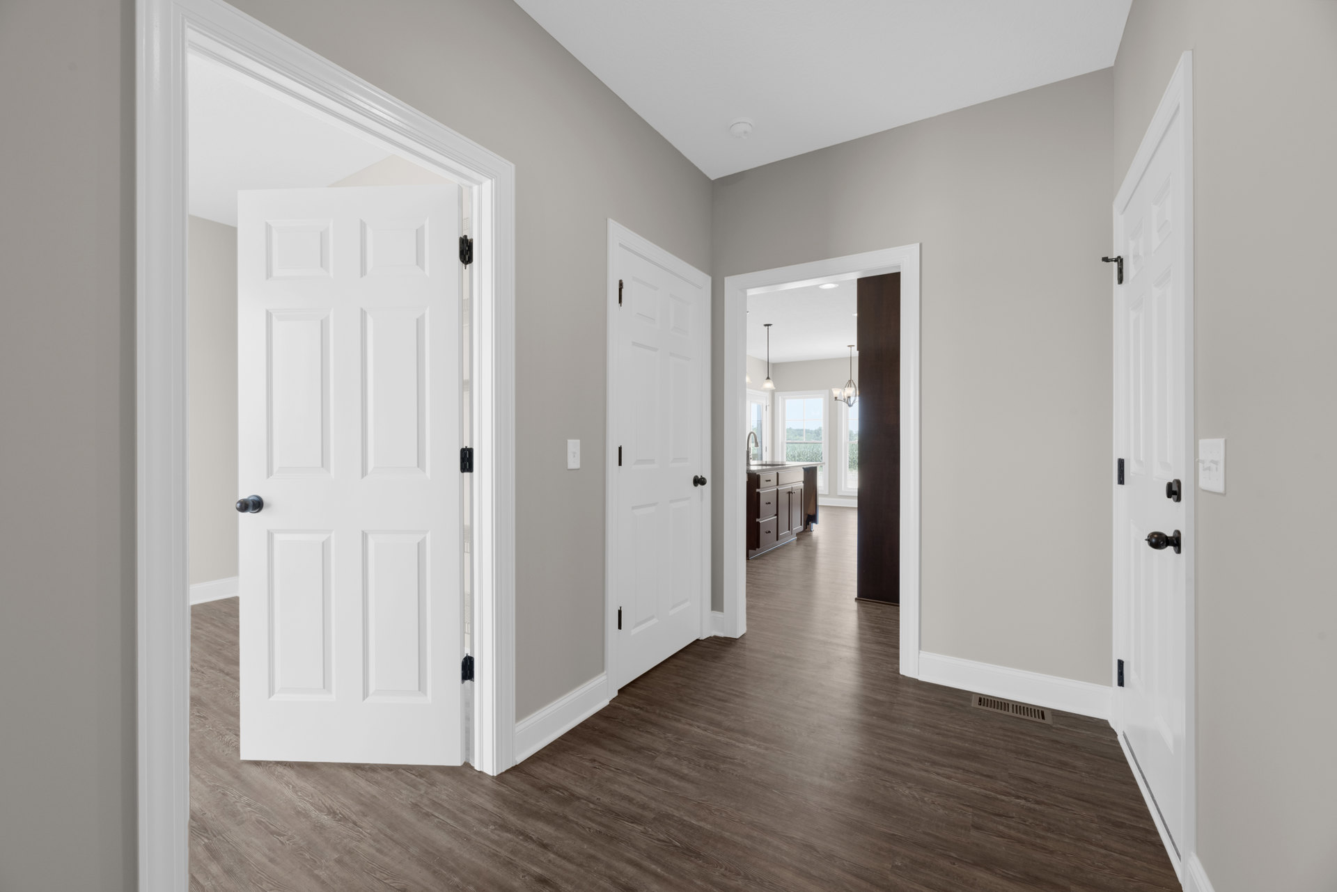 Hallway with white paneled doors, black door knobs, and dark brown wood flooring