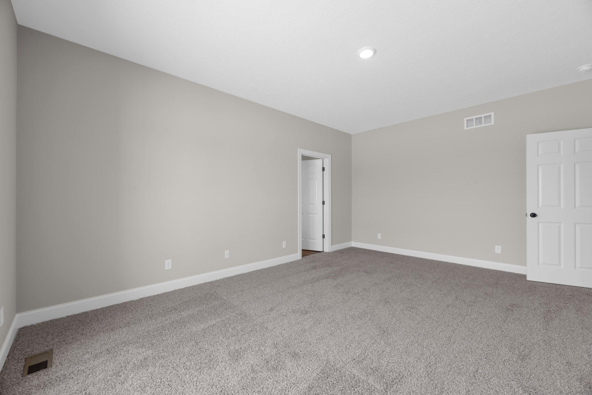 Neutral-toned carpeted room with white walls, white door featuring a black handle, ceiling and wall vents visible