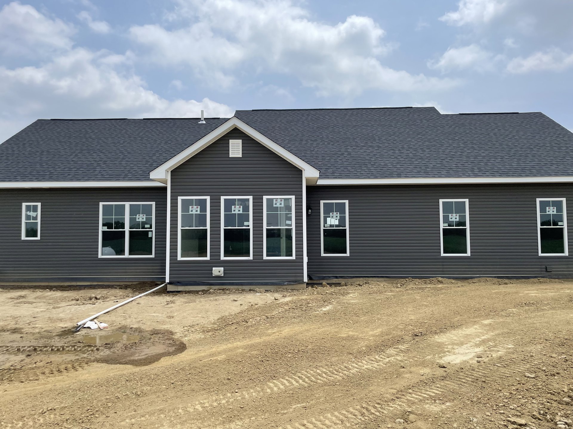 Two-story house under construction with white framed windows, exposed siding, and dirt foreground under a blue sky with scattered clouds