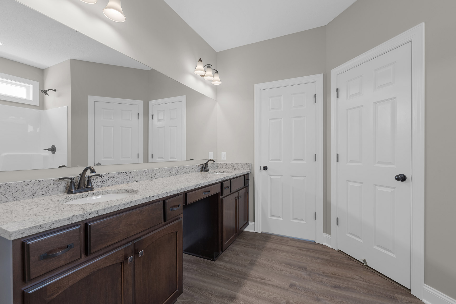 Bathroom with double vanity featuring white cabinets and marble countertop, two undermount sinks with chrome faucets, white paneled doors with black knobs, and a three-light