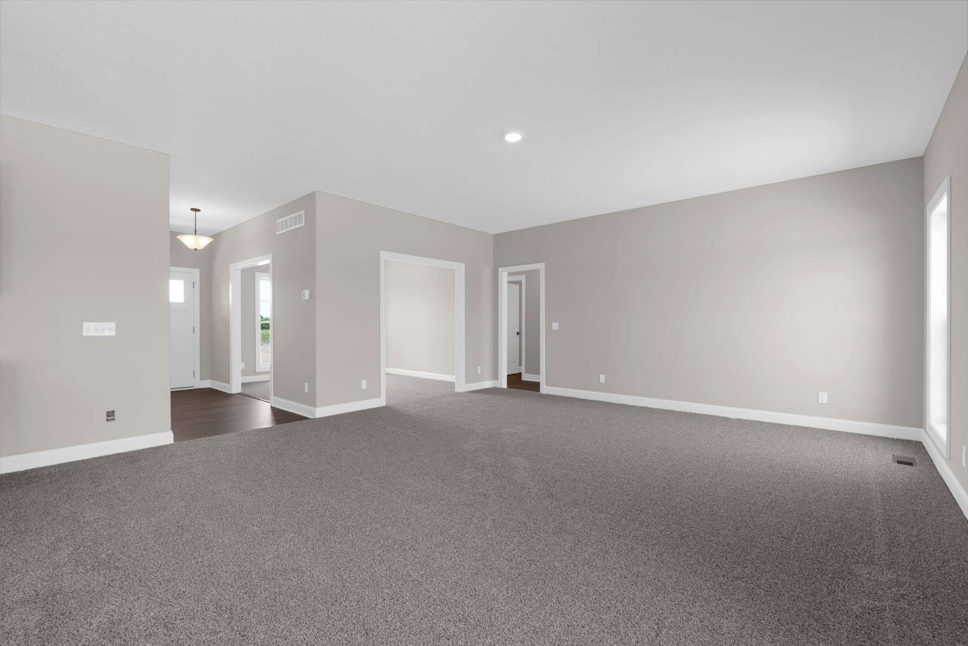 Neutral-toned carpeted room with white painted walls, open white door featuring black knob, simple ceiling-mounted light fixture, and smooth plaster ceiling.