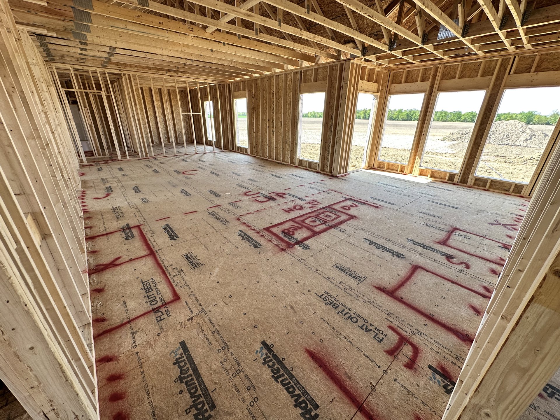 Room with exposed wooden ceiling beams, large windows, and red writing marked across a tiled floor