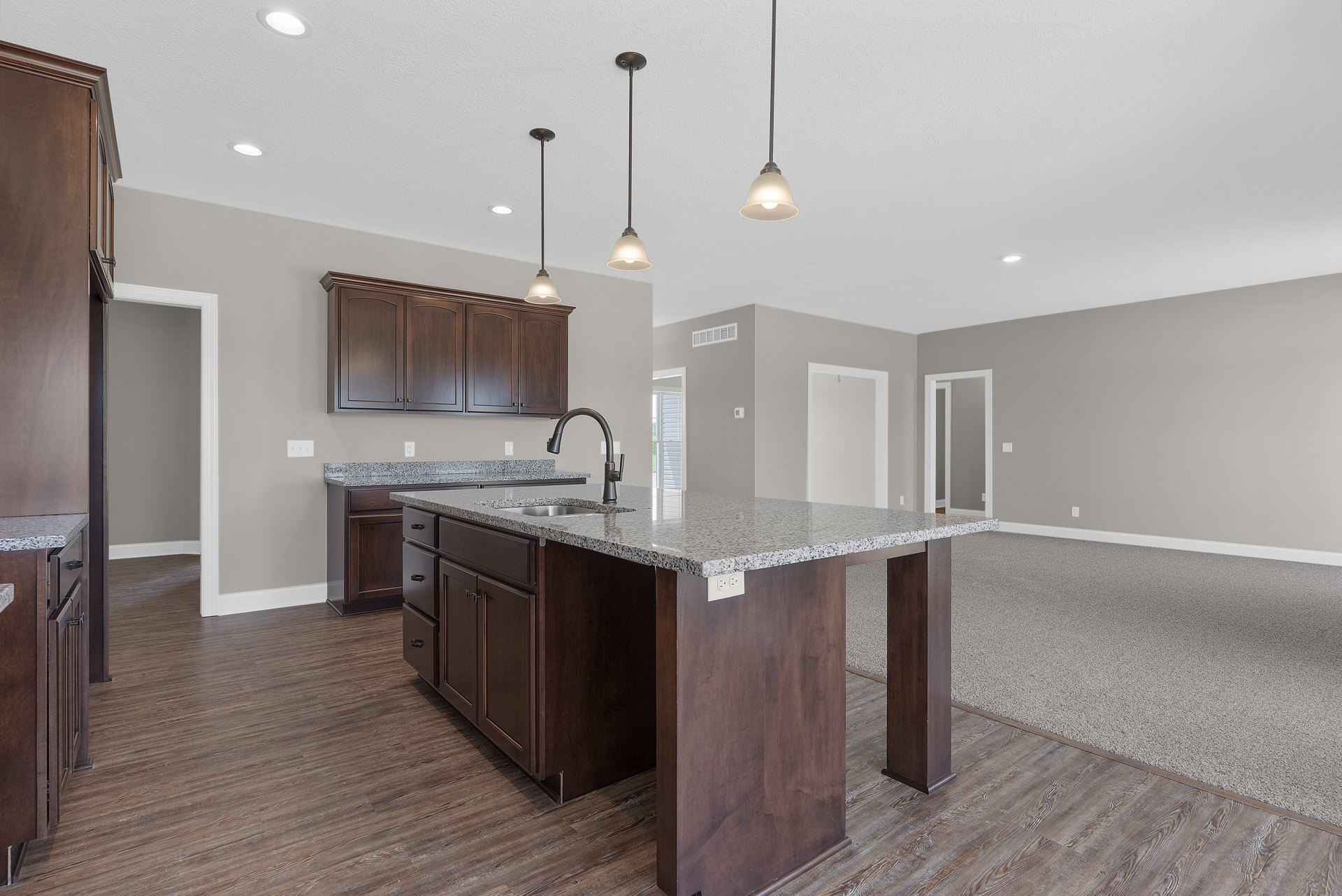Spacious kitchen featuring a large central island with granite countertops, tile flooring, white cabinetry, stainless steel sink, and modern appliances.