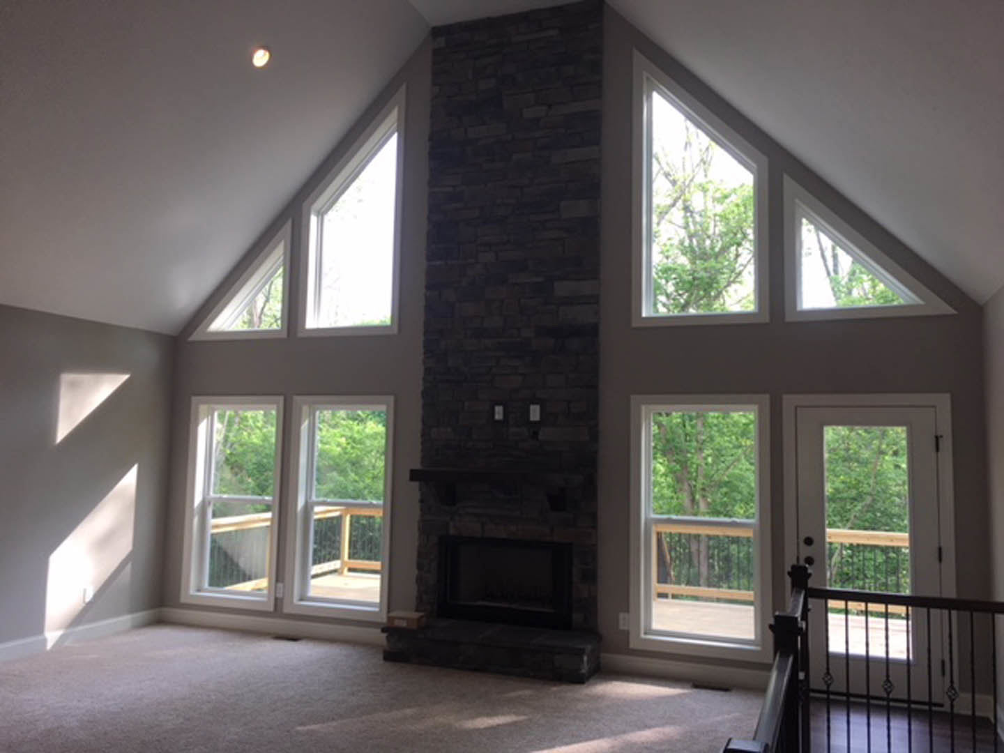 Living room featuring a brick fireplace, large windows with tree views, hardwood floors, and a modern chair near a paneled door.