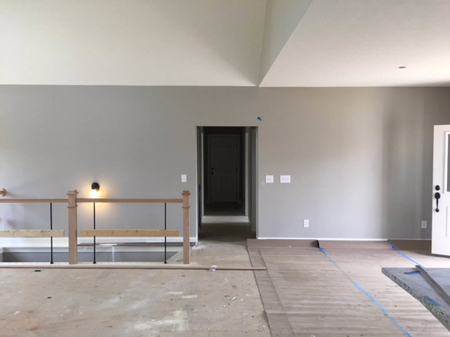 Open-concept room featuring two staircases with metal railings, concrete flooring, white plaster walls, wooden door, and wall-mounted light fixture