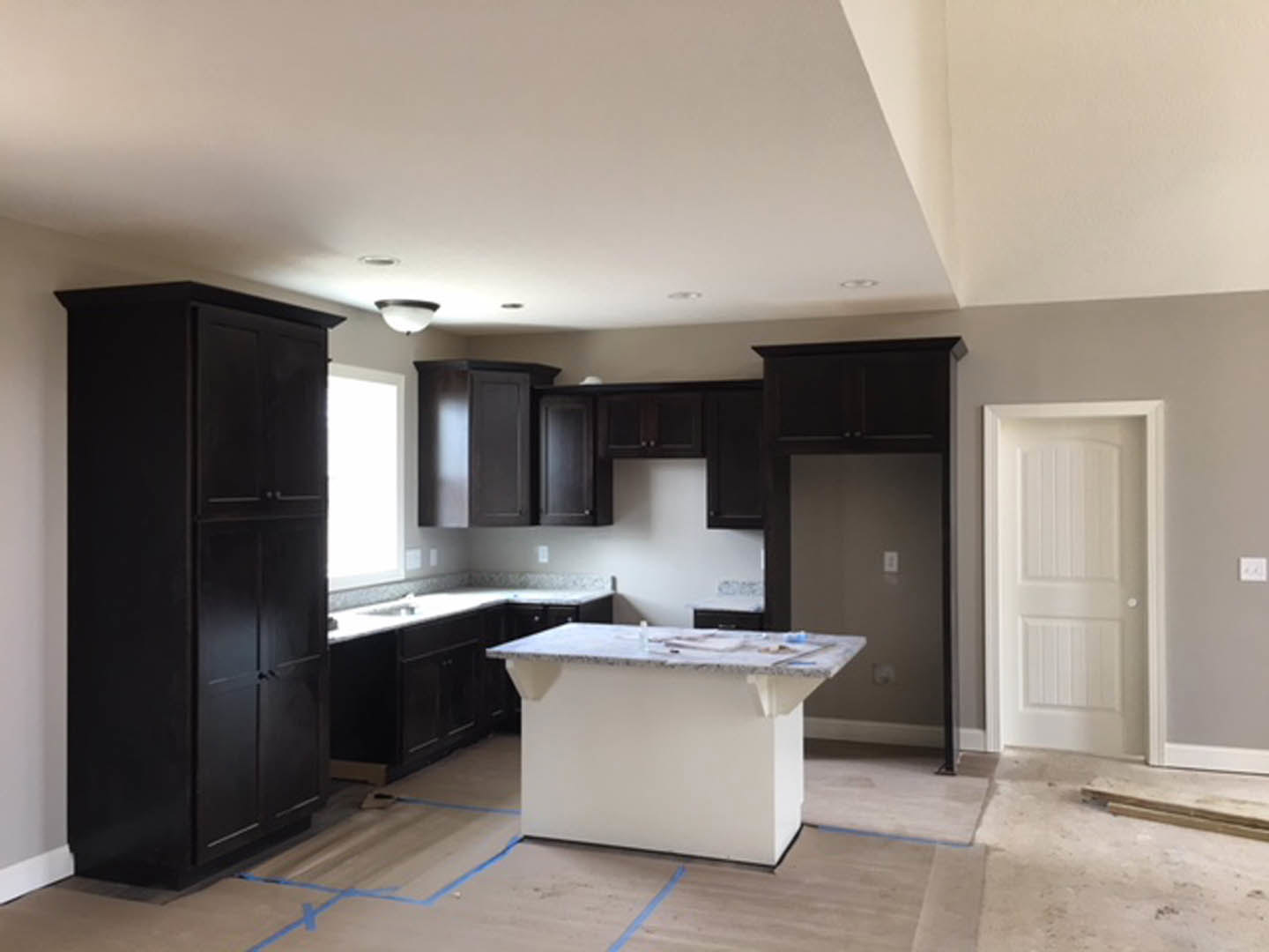 Kitchen featuring dark wood cabinets, white marble-topped island, tile flooring, stainless steel sink, and light walls with a white door and light switch