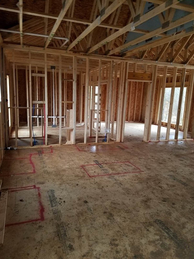 Wood-framed room under construction with exposed beams, ceiling trusses, and red lines marked on the concrete floor.