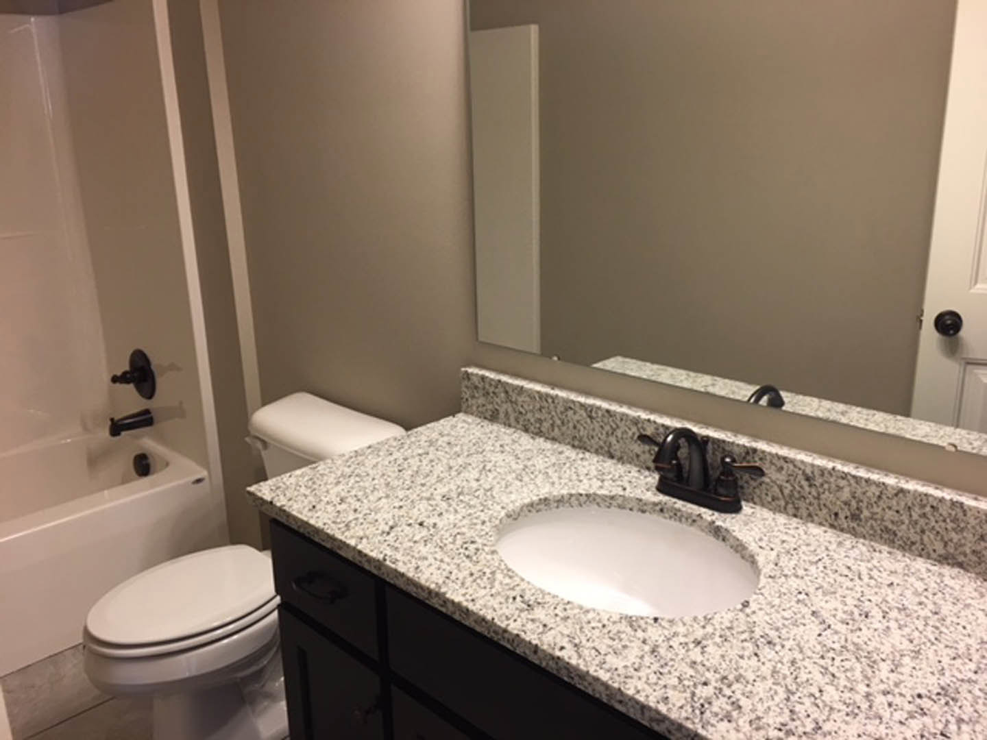 White porcelain sink with matte black faucet, adjacent toilet with closed lid, light tile flooring, neutral wall tiles, and minimalist bathroom accessories