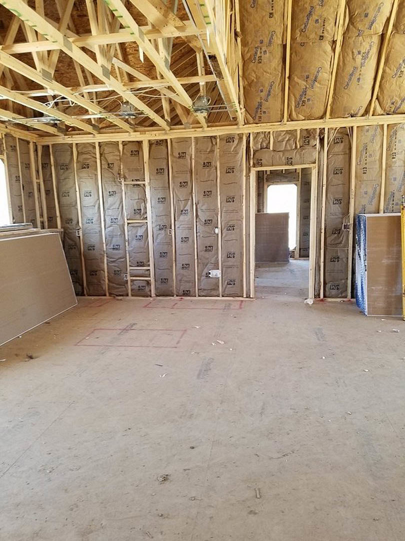 Open-concept room featuring exposed wooden ceiling beams, white walls, and a large window framed in brown trim, with construction materials visible.